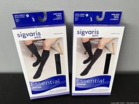 Front view of two boxes of Sigvaris Men Essential Cotton black knee-high compression socks, size LL, 20-30 mmHg compression.