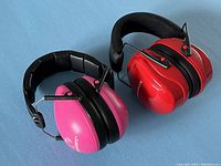 Two pairs of children's ear muffs for hearing protection, one red branded Range Maxx and one pink branded Walkers, lying side by side.