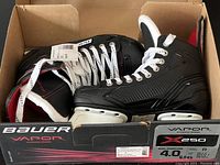 Pair of Bauer Vapor X250 junior hockey skates in original box, viewed from above showing left skate with tag attached and right skate partially visible.