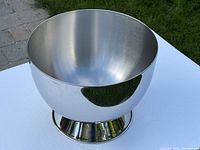 Polished stainless steel wine/champagne bucket shown from above angle on table outdoors with grass in background.