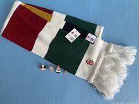 Full view of folded Hudson's Bay wool scarf with tags and four Olympic pins laid out at base on blue background