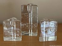 Front view of all three clear glass triangular candle holders arranged side by side on wooden surface varying in size with bubble textured interiors