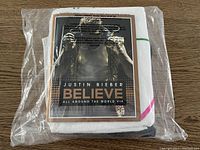 Justin Bieber Believe Tour towel and tour book sealed inside plastic wrapping on wooden surface.