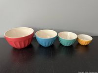 Front view of the four ceramic mixing bowls arranged largest to smallest showing colors and fluted exterior.