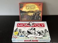 Photo of Monopoly classic edition and Settlers of Catan base game boxes placed side by side on a flat surface.