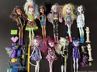 Ten Monster High dolls arranged horizontally with assorted accessories including shoes, bags, necklaces, and several small plastic pets.