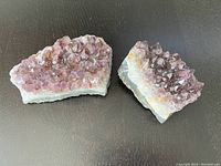 Two natural purple amethyst crystal clusters placed on a dark surface, showing top and side views with crystal points and base visible.