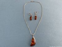 Full view of sterling silver necklace with amber pendant and matching amber earrings on a grey surface.