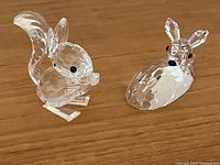 Close-up front angle photo showing the Swarovski faceted crystal squirrel and lying deer fawn figurines on a wooden surface.