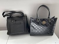Front view of two black handbags side by side, one with quilted design and gold hardware handles, the other with smooth surface and front zipper pocket.