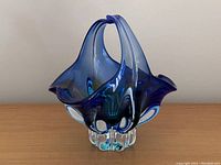 Side angle front view of vintage blue hand blown glass bowl showing glossy deep blue and clear glass with ruffled rim and integrated handle.