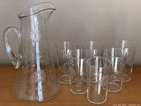 Full view of the vintage clear glass pitcher alongside six matching glasses, showing overall condition and etching pattern