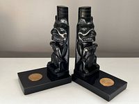 Pair of black carved argillite Haida bookends showing front and side angles, with brass medallions on rectangular bases