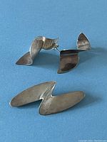 Photo showing two wave-shaped sterling silver earrings and one matching abstract brooch on blue background.