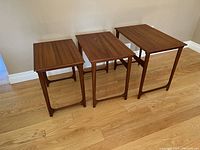 Three teak nesting tables displayed side by side on hardwood floor
