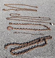 All five chains laid out on asphalt showing different lengths and weights, including a large hook at one end