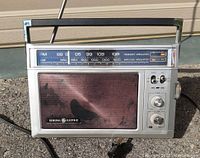 Front view of General Electric AM/FM radio showing tuning dial, speaker grill, control knobs, toggle switches, and antenna.