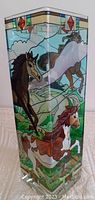 Front side of vase featuring multiple horses painted in stained glass style with green fields and blue sky background