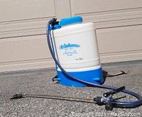 White and blue Friulna 5 litre backpack sprayer with black straps and blue cap sitting on the ground, hose and spray wand extended.