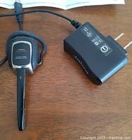 Jabra Supreme Bluetooth headset with wall charger on a wooden surface, showing the headset's design and charger plug.