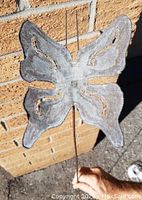Metal butterfly lawn decoration held upright against a brick background, showing wing shape and detailing.
