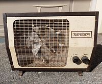 Front view of Torcan heater/fan unit showing metal grille, heating coil and fan blades, control knobs and brand logo.