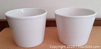Two white ceramic flower pots side by side on a table, showing their size and shape