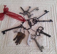 Overview of assortment of vintage skeleton keys, clock winding keys and cast iron keys on quilted fabric, with one key tied with red ribbon.