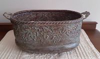 Full view of rectangular vintage copper pot with etched grape design, showing handles and aged patina.