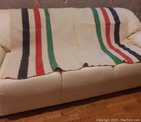 Rolled out view of the full blanket showing its colored stripes and cream background on a white couch.