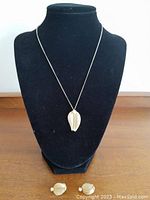 Full view of the pendant on a chain displayed on a black velvet jewelry display bust with matching screw back earrings placed below.