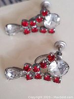 One earring laying flat showing red square rhinestones and clear teardrop rhinestone with screw back attachment.