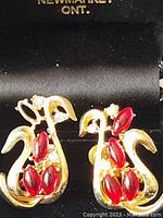 Front view showing gold tone clip-on earring with red and clear rhinestones.