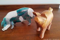 Photo of two pig figurines: a multicolored ceramic pottery pig and a smooth wooden carved pig figurine.