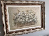 Front view of framed floral art print showing white flowers in a wooden container with neutral background and ornate gold-tone scalloped frame.