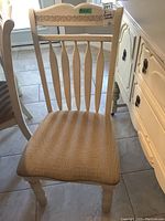 Front view of chair showing leaf design on top rail, vertical back slats, and upholstered seat.