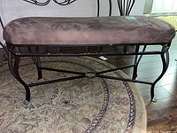 Side view of bench showing brown cushioned top and black metal frame with curved legs and cross-support bars.