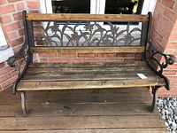 Front view of cast iron and wood bench showing floral pattern on backrest and weathered wood slats.