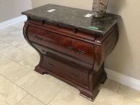 Front view of mahogany bombe style cabinet with stone top showing four drawers with metal handles and carved detailing
