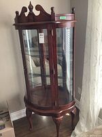 Full view of the mahogany curio cabinet showing front curved glass door, side glass panels, finial decorative top, and carved legs.