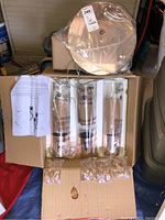 3-light chandelier components in a box, including metal ceiling mount base, three vertical glass tubes with hanging teardrop glass pendants, small glass pendants in plastic bags, and instruction manual.