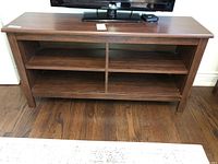 Front view of rectangular faux wood console table with four open compartments, showing wear on the surface.