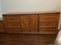 Front view of wooden dresser showing six drawers and central cabinet with double doors, medium brown finish, visible scratches.