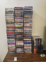 Large stack of about 100 DVD cases including various movie titles and TV series box sets piled side-by-side on a wooden surface against a white wall.