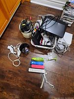 Overview of Wii console, cords in baskets, Sony BDP-S1100 DVD player stacked on console, multiple game controllers laid out on floor.