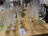 View of 11 clear Cristal D'Arque crystal champagne flutes with vertical cuts on the bowls and stems, arranged on a wood table.