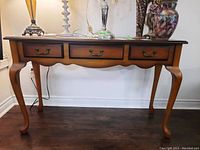 Front view of wooden hall table with three drawers, showing the cabriole legs and tabletop surface with minor scratches.