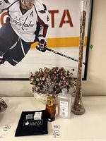 Wide view showing Lampe Berger lamp with refill, artificial pink roses in separate cluster, and tall glass vase filled with pennies.
