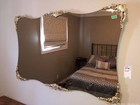 Front view of the large rectangular mirror with curved edges and ornate gold-tone decorations on each corner, showing clear reflection of bedroom.