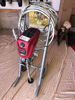 Front angle view of Titan ControlMax 1700 Pro paint sprayer mounted on metal cart with large hose coiled around frame, showing condition and wear.